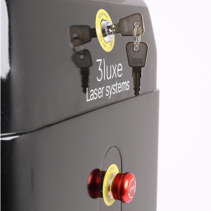 Close-up of a black 3Luxe Laser Systems enclosure showing a lock with keys, a red and yellow emergency stop button,